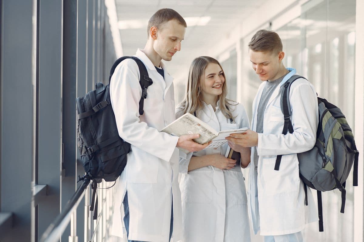Medical students in white coats reviewing notes together in a hospital corridor.
