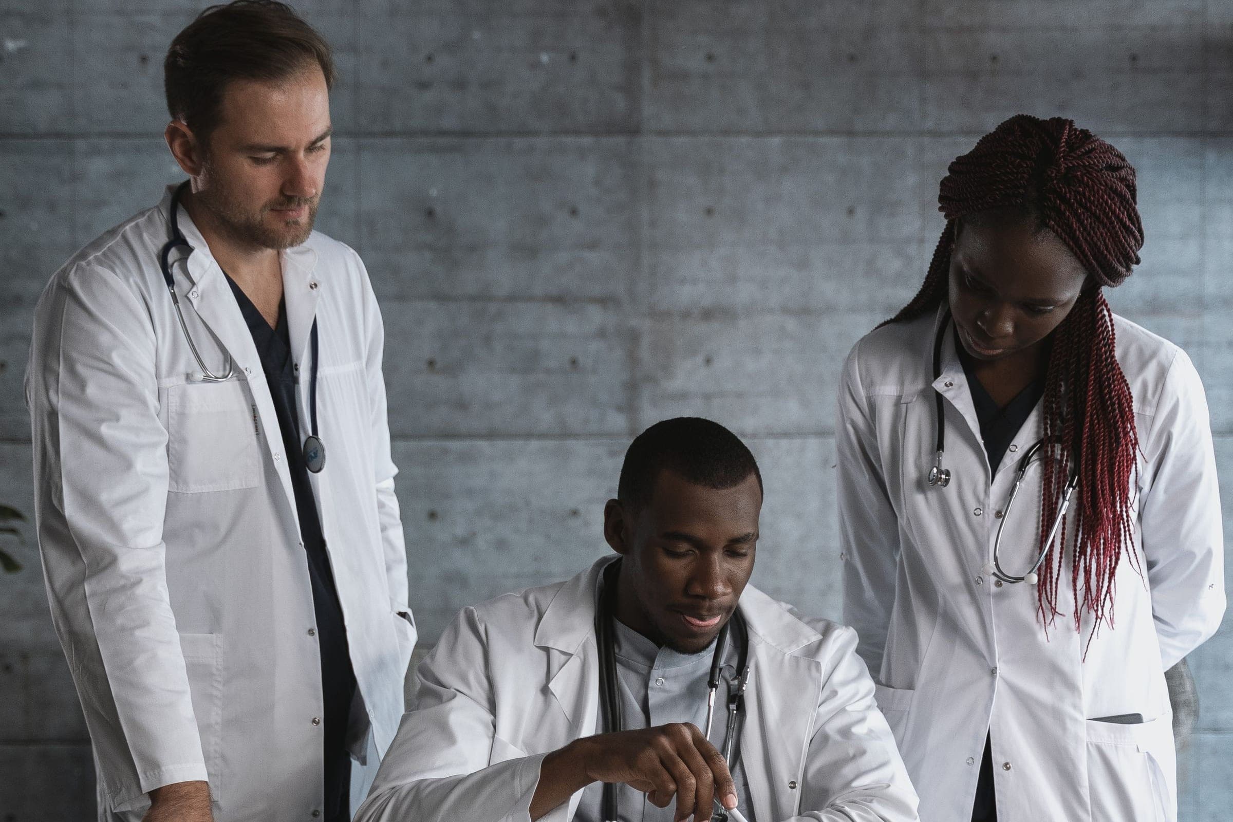 Two clinicians standing over a colleague at a desk, working through a case together.